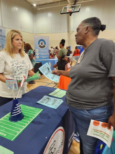 Two women exchanging flyers at an indoor event.