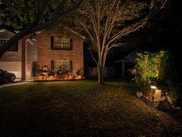 A warmly lit brick house with a tree and garden at night.