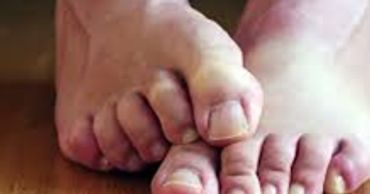 Close-up of toes on wooden floor, one foot overlapping the other.