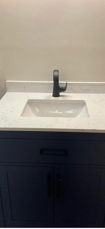 Modern bathroom vanity with dark blue cabinet and white marble countertop.