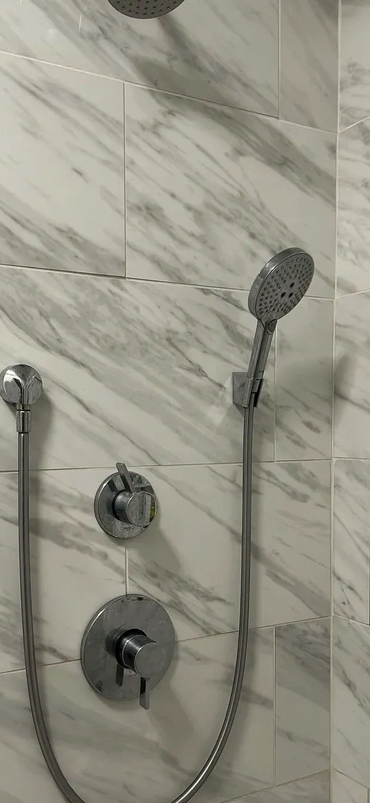 Modern shower with marble tiles and a handheld showerhead.