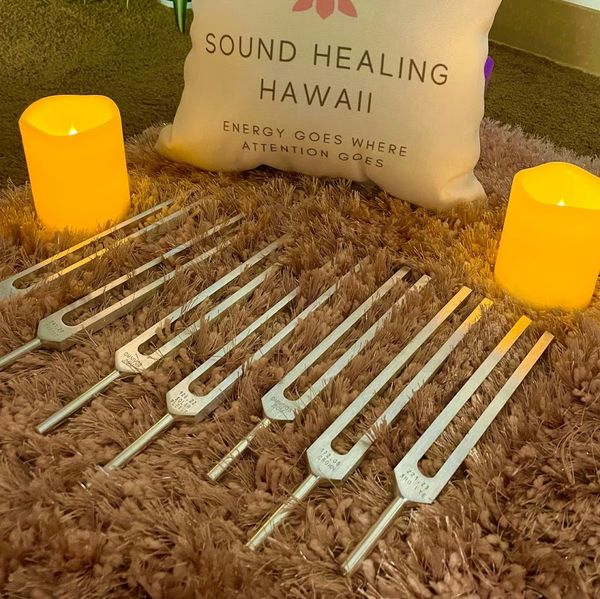 seven chakra aligned tuning forks on a pink carpet in between candles for sound bath session.