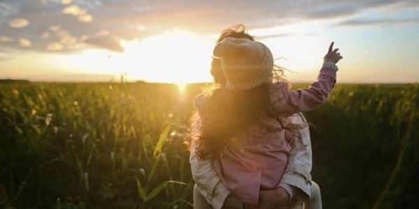 A woman holding a child in a grassy field.