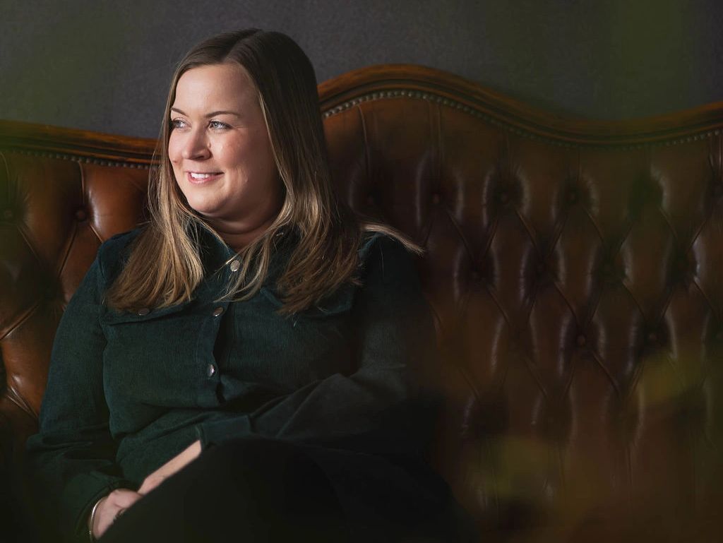 Woman smiling while sitting on a brown leather sofa.