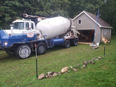 Concrete mixer truck parked beside a small garage in a grassy area.