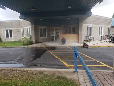 Person cutting concrete near building entrance, surrounded by dust.