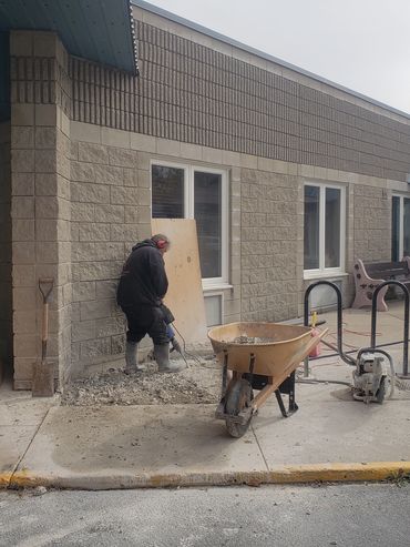 Worker using a jackhammer on concrete outside a building under construction.