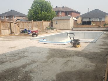Backyard under construction with an empty pool and gravel ground preparation.