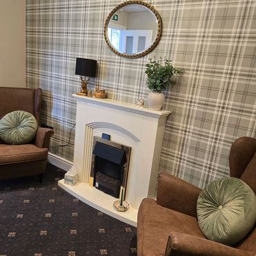 Cozy living room with plaid wallpaper, brown armchairs, and a white fireplace with decorative items.