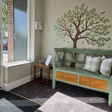 Cozy corner with a green bench, bird mural, and sunlight streaming through a large window.