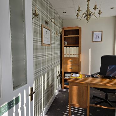 Sunlit office with wooden furniture and plaid wallpaper.