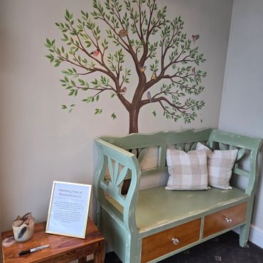 Cozy corner with a green bench, plaid pillows, and a painted memory tree on the wall.