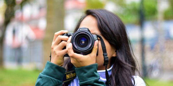 Person holding a Nikon camera, taking a photo outdoors.