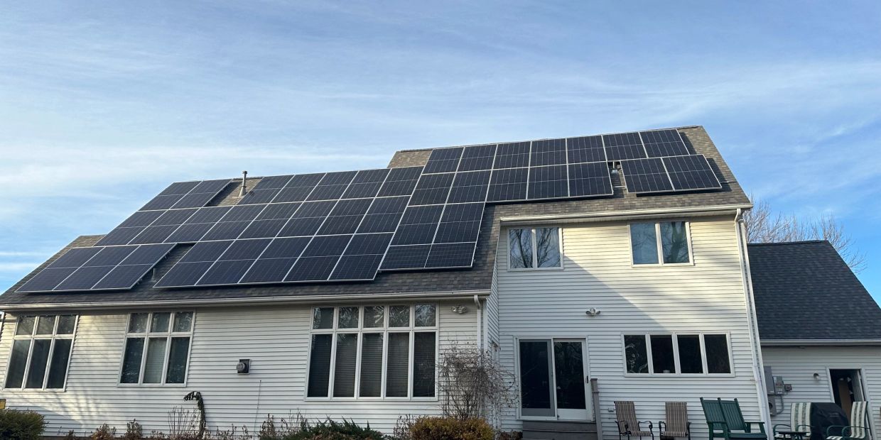 Large house roof covered with multiple solar panels under a clear sky.