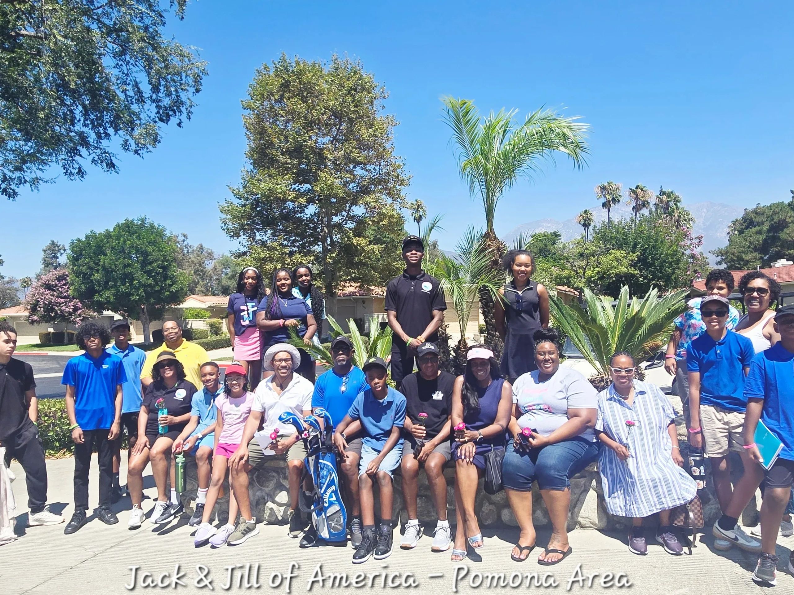 A large group of people posing outdoors with palm trees and clear blue sky.
