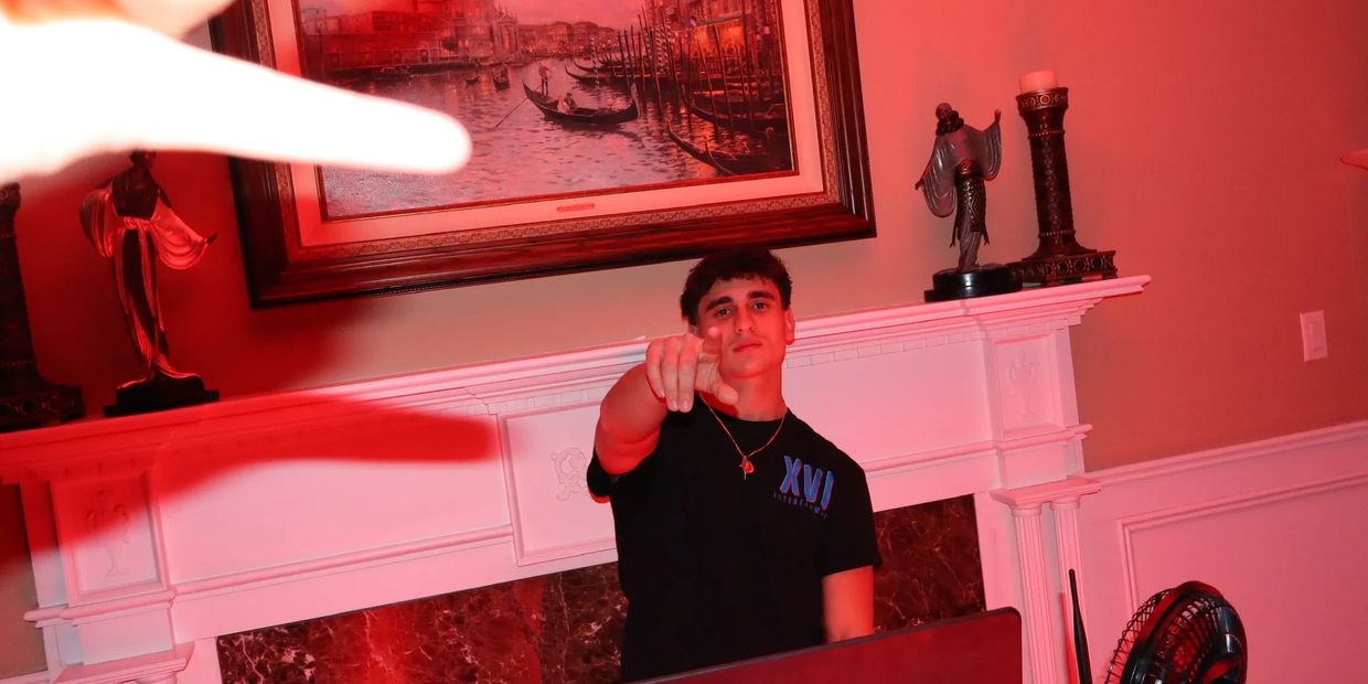 Young man points at the camera in a red-lit room with a fireplace and art.
