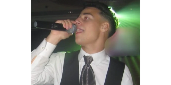 Young man singing into a microphone at an event, dressed formally.