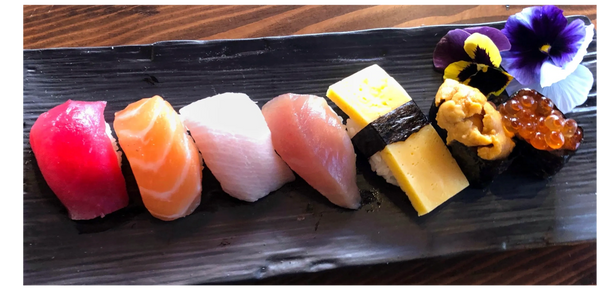 7 pieces of sushi on a dark wooden plate