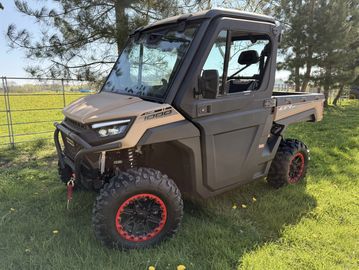 A rugged off-road utility vehicle parked on grass near a fence and trees.