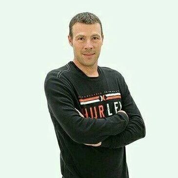 Man in a black sweater with arms crossed, smiling.