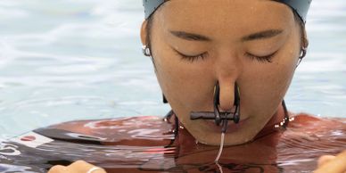 A swimmer wearing a nose clip and swim cap with eyes closed in water.