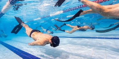 Underwater swimmers wearing fins and swim caps in a pool.