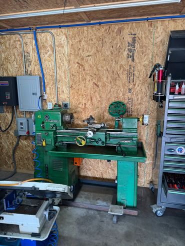 A green Clausing lathe machine in a workshop with tool storage and a fire extinguisher.