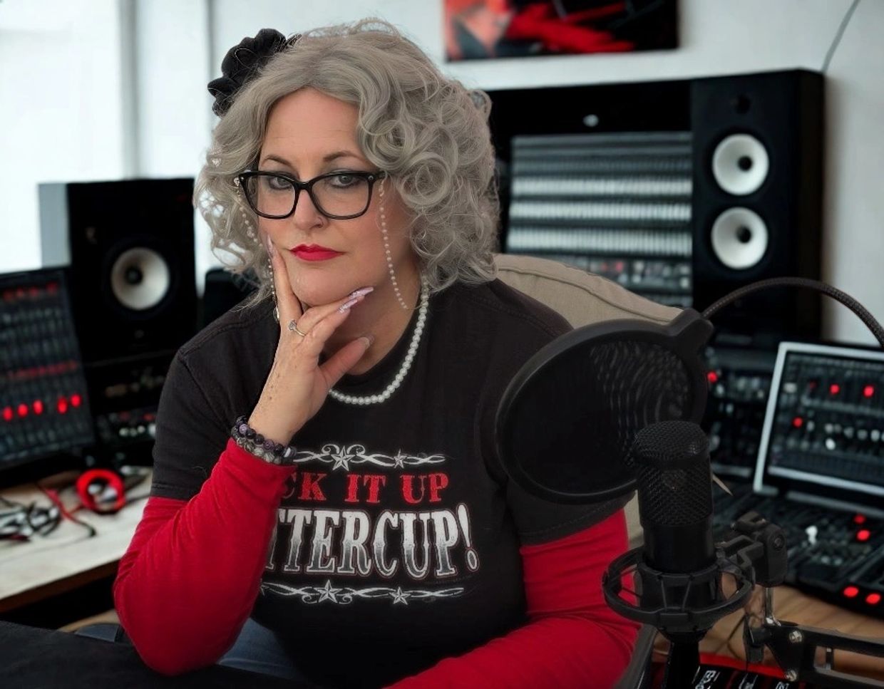 Woman with gray curly hair and glasses in a recording studio.