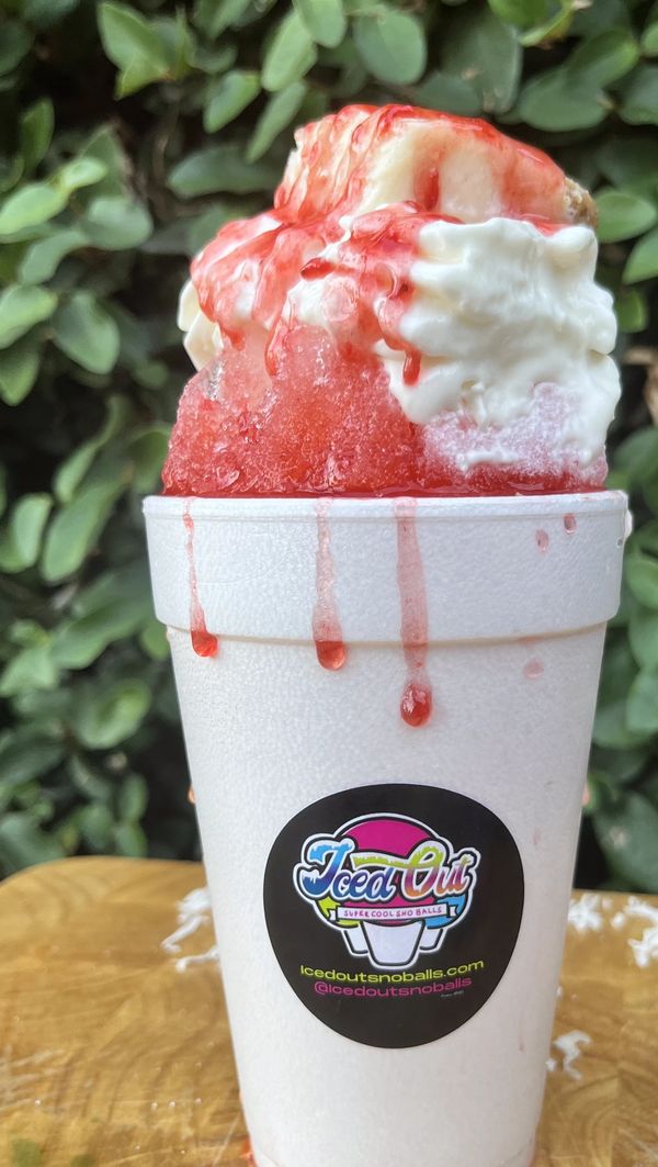 A vibrant red snowball treat with whipped cream in a white cup.