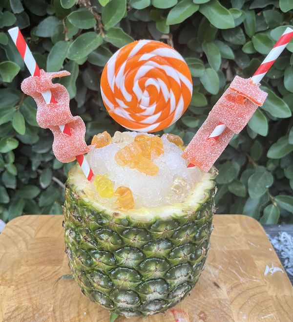 A pineapple filled with crushed ice, gummy bears, candy straws, and a large orange swirl lollipop.