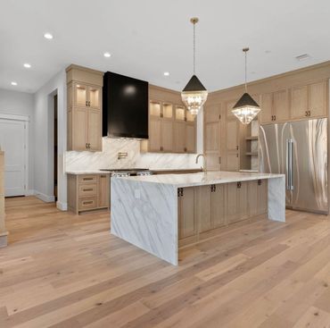 Modern kitchen with marble island, wooden cabinets, and stainless steel appliances.
