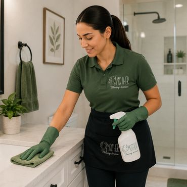 A woman in green uniform cleaning a bathroom countertop.