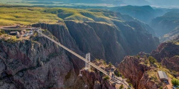 A long suspension bridge stretches across a deep canyon under a blue sky.