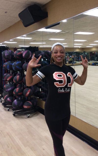 Smiling woman in workout clothes posing in a gym.