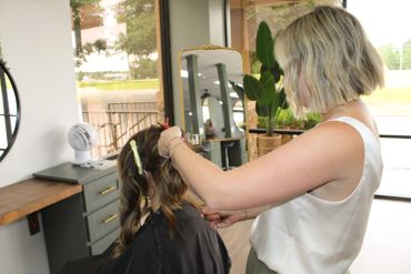 A hairstylist styling a client's hair in a bright salon.