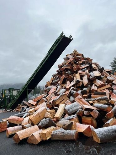 Pile of cut firewood dusted in snow. A mechanical firewood processor over top of it