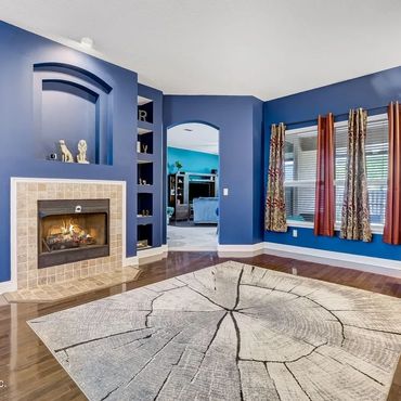 Cozy living room with blue walls, built-in shelves, fireplace, and large window draped with patterned curtains.