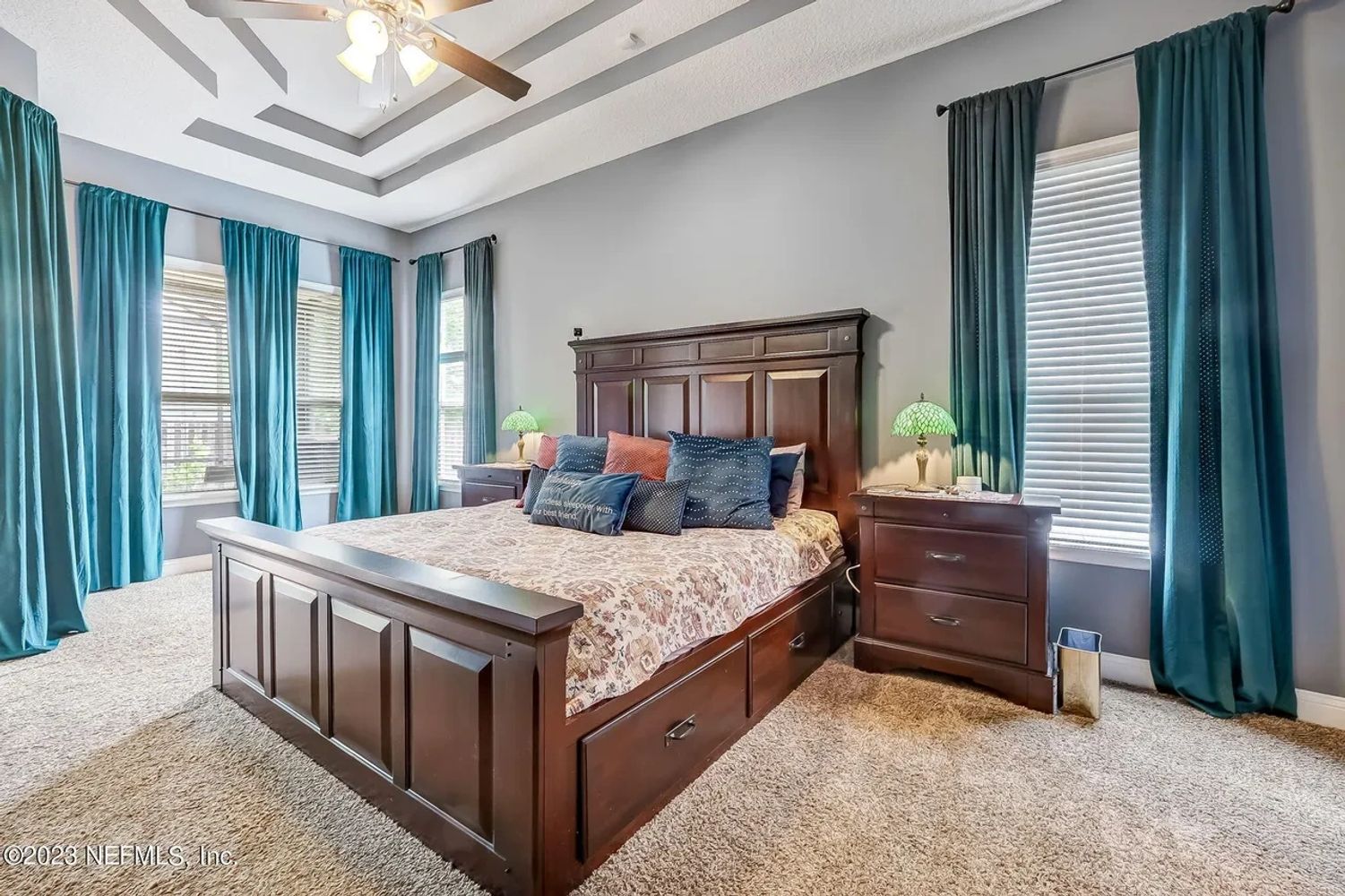 Spacious bedroom with a wooden bed, teal curtains, and cozy carpeting.