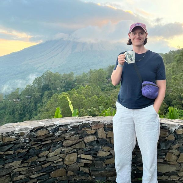 Person enjoying a drink with a mountain view and cloudy sky.