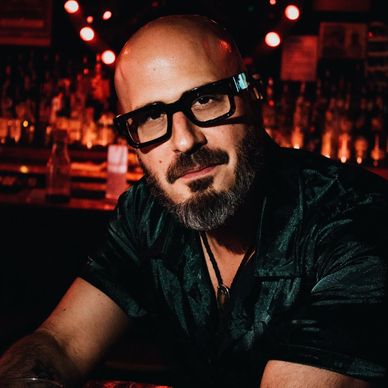 Bearded man wearing glasses in a dimly lit bar.
