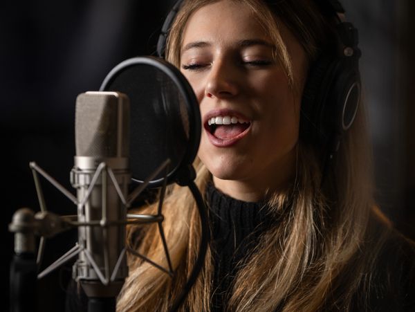Woman singing into a microphone with headphones on.