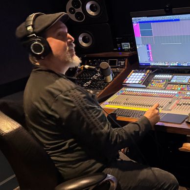 Man working in a sound studio with headphones and mixing console.