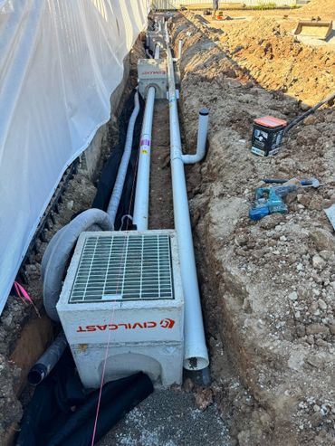Construction site with drainage pipes and concrete catch basins being installed.