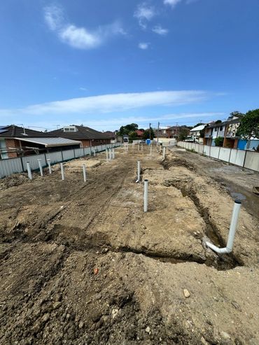 Construction site with plumbing pipes installed in the ground under a blue sky.