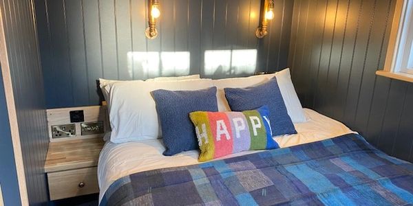 Cozy bed with colorful pillows and blue quilt in a warmly lit room.