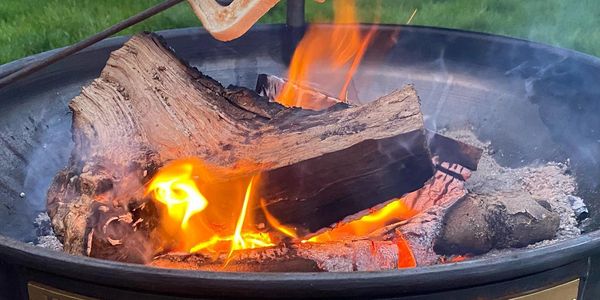 Wood logs burning brightly in a fire pit outdoors.