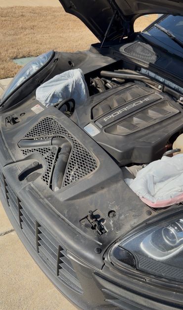 Open hood of a Porsche showing a dusty engine compartment.