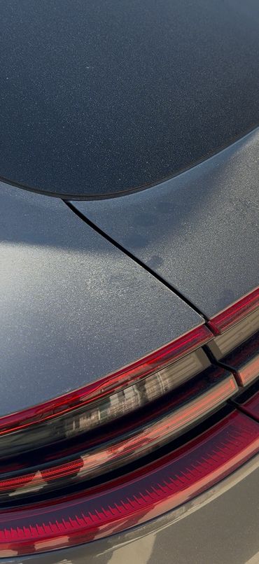 Close-up of a gray Porsche's rear tail light and back window on a sunny day.