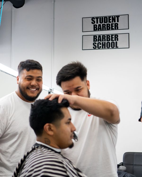 Instructor guiding a student while cutting a client’s hair, both enjoying the training experience.