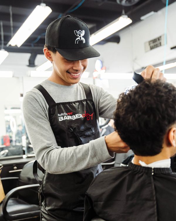 Barber School student smiling while cutting a client’s hair and enjoying hands-on training.